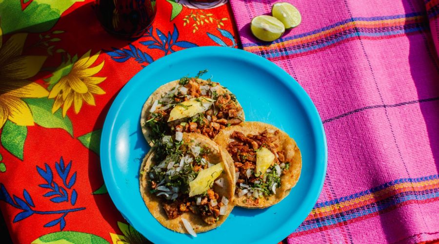 A vibrant blue plate with three tacos topped with onions, cilantro, and avocado, served on a colorful floral tablecloth